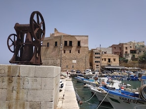 Un poble costaner amb un edifici històric, una noria i un port esportiu amb vaixells.