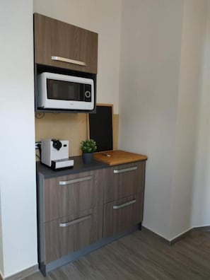 A compact kitchenette with a microwave, a small coffee maker, and a wooden cutting board.