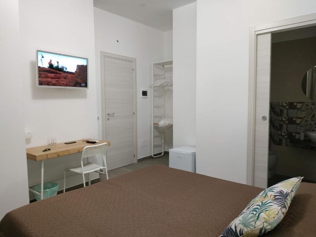 Una camera da letto con un letto, una scrivania, una sedia, una TV, un armadio e una piccola credenza bianca.