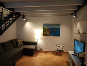 Un saló amb un sofà, una taula petita, una televisió, un quadre i una escala.