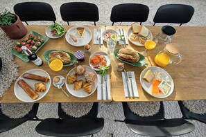 Uma mesa de jantar com diversos itens de café da manhã, como doces, frutas e bebidas.
