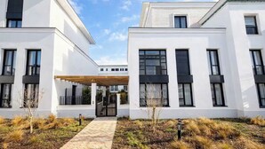 Ein modernes Gebäude mit weißen Außenwänden, zahlreichen Fenstern und einem überdachten Eingang.