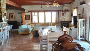 A rustic interior with a stone fireplace, wooden beams, a dining area, and a white wall with a mounted saddle. - Sun Holiday Kea Private Pool Sea View (Kea)