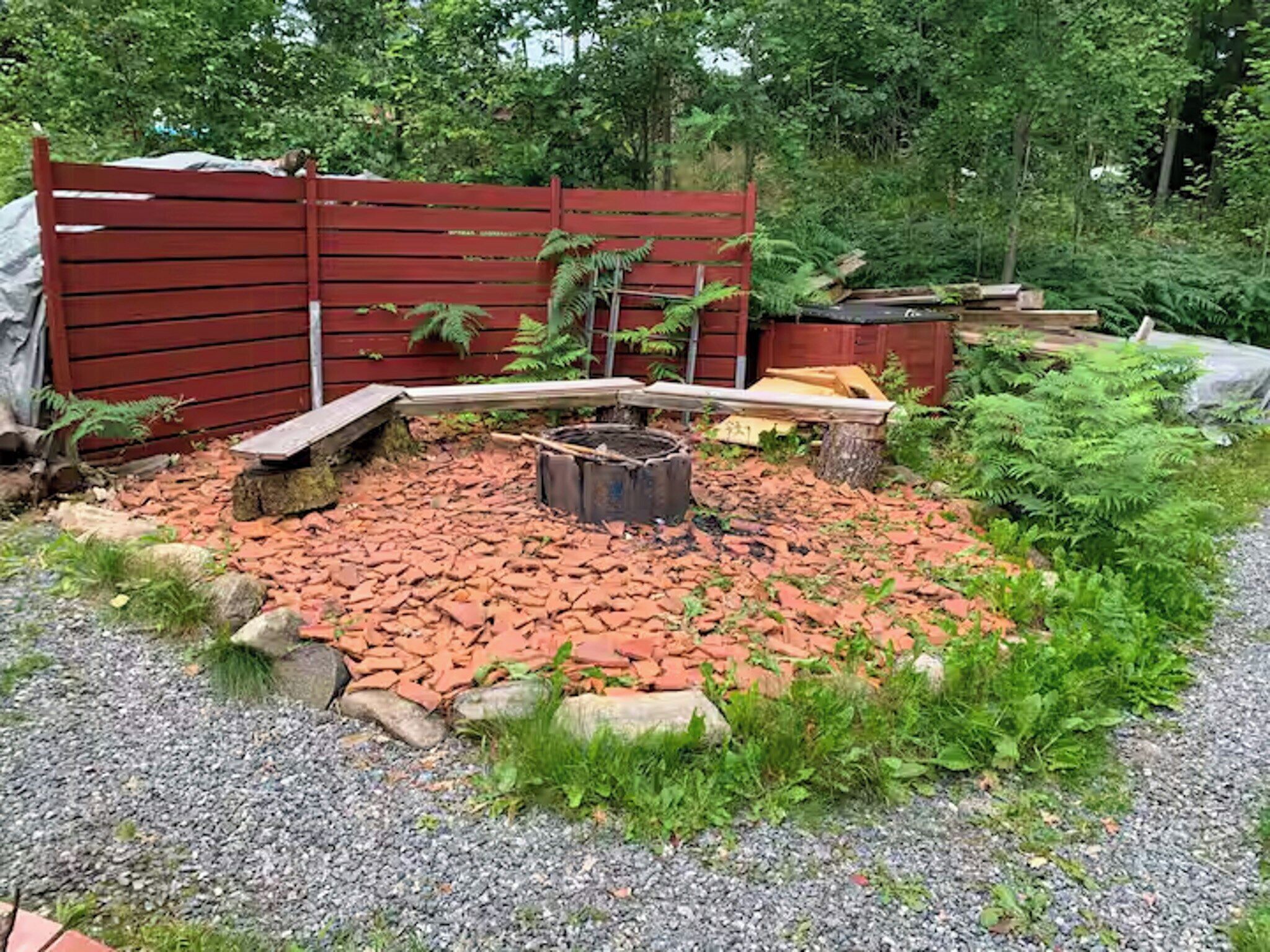 A garden with a fire pit, red wooden fence, and various plants.