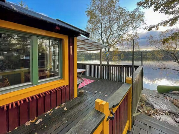 Una cabaña con terraza con vistas a un lago, un espacio cubierto y vistas a árboles y agua.