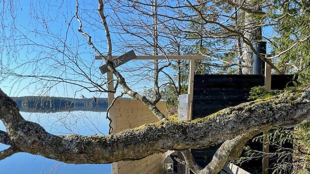 A wooden dock extending over a calm lake, with a bench and a small structure on the right. - Lakeside cabin with paddle board (Lerum)
