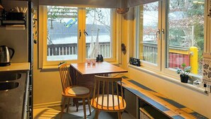 A kitchen with a dining table, chairs, a stove, and a window with a view of a deck and trees. - Lakeside cabin with paddle board (Lerum)