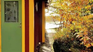 A green door with a window, a yellow and red wall, and a garden with autumn foliage. - Lakeside cabin with paddle board (Lerum)