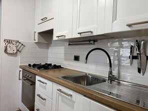Une cuisine avec des armoires blanches, un plan de travail en bois, un évier en acier inoxydable et une cuisinière à gaz.