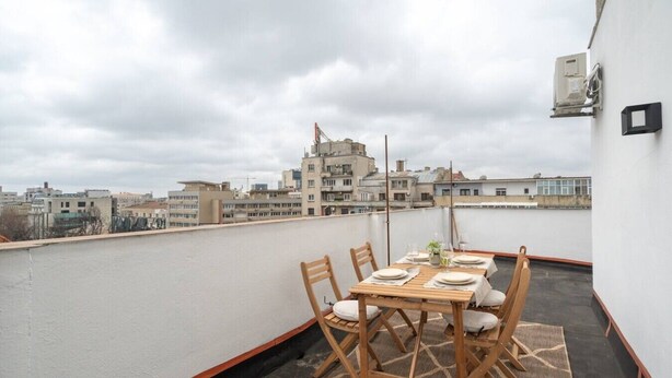 En tagterrasse med et bord dækket til to, omgivet af stole, og udsigt over bybilledet.