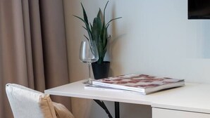 En moderne kontorstol med pude, et skrivebord med plante og et magasin, og et TV ophængt på væggen.