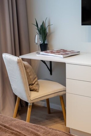 Ein moderner Bürostuhl mit Polster, ein Schreibtisch mit Pflanze und Zeitschrift sowie ein an der Wand befestigter Fernseher.