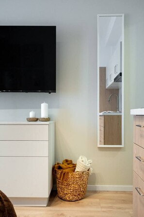 Ein modernes Zimmer mit einem wandmontierten Flachbildfernseher, einer weißen Kommode, einem Korbwäscheschrank mit Handtüchern und einem großen Spiegel.