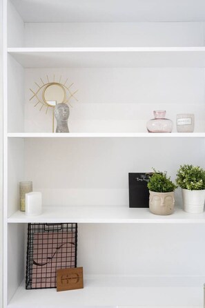 Ein weißes Regal mit Dekorationsobjekten, darunter ein sonnenähnliches Objekt, eine rosa Vase und Topfpflanzen.