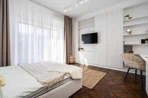 Ein modernes Schlafzimmer mit Bett, Schreibtisch, Stuhl, Fernseher und einem Fenster mit Vorhängen.