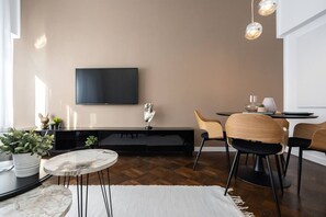 A modern living room with a flat-screen TV, wooden chairs, a marble coffee table, and a dining area with a small table and chairs. - Luxury 2-Room Apartment | Central (Bucharest)