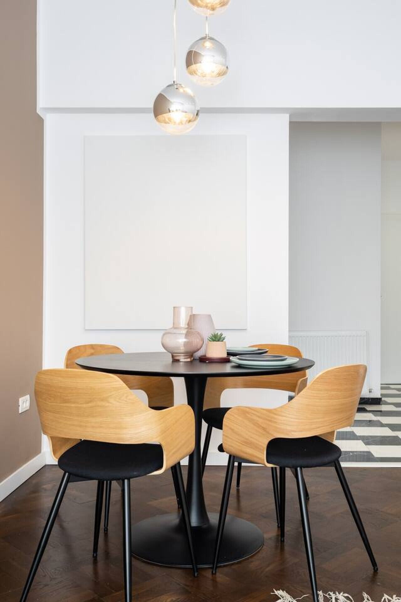 A dining area with a round table, four wooden chairs, a vase, and a potted plant.