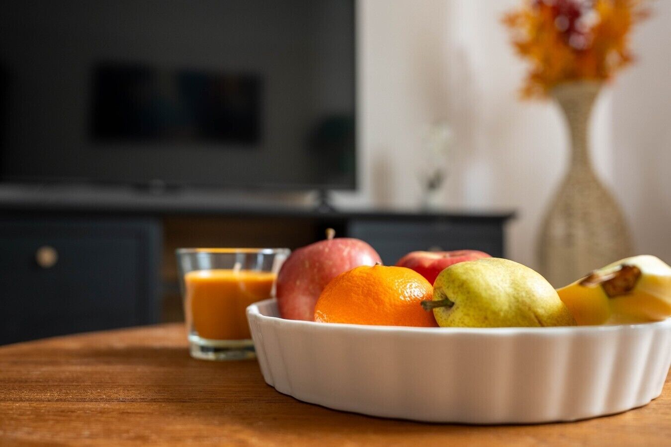 A bowl of fruit on a table with a glass of orange juice.