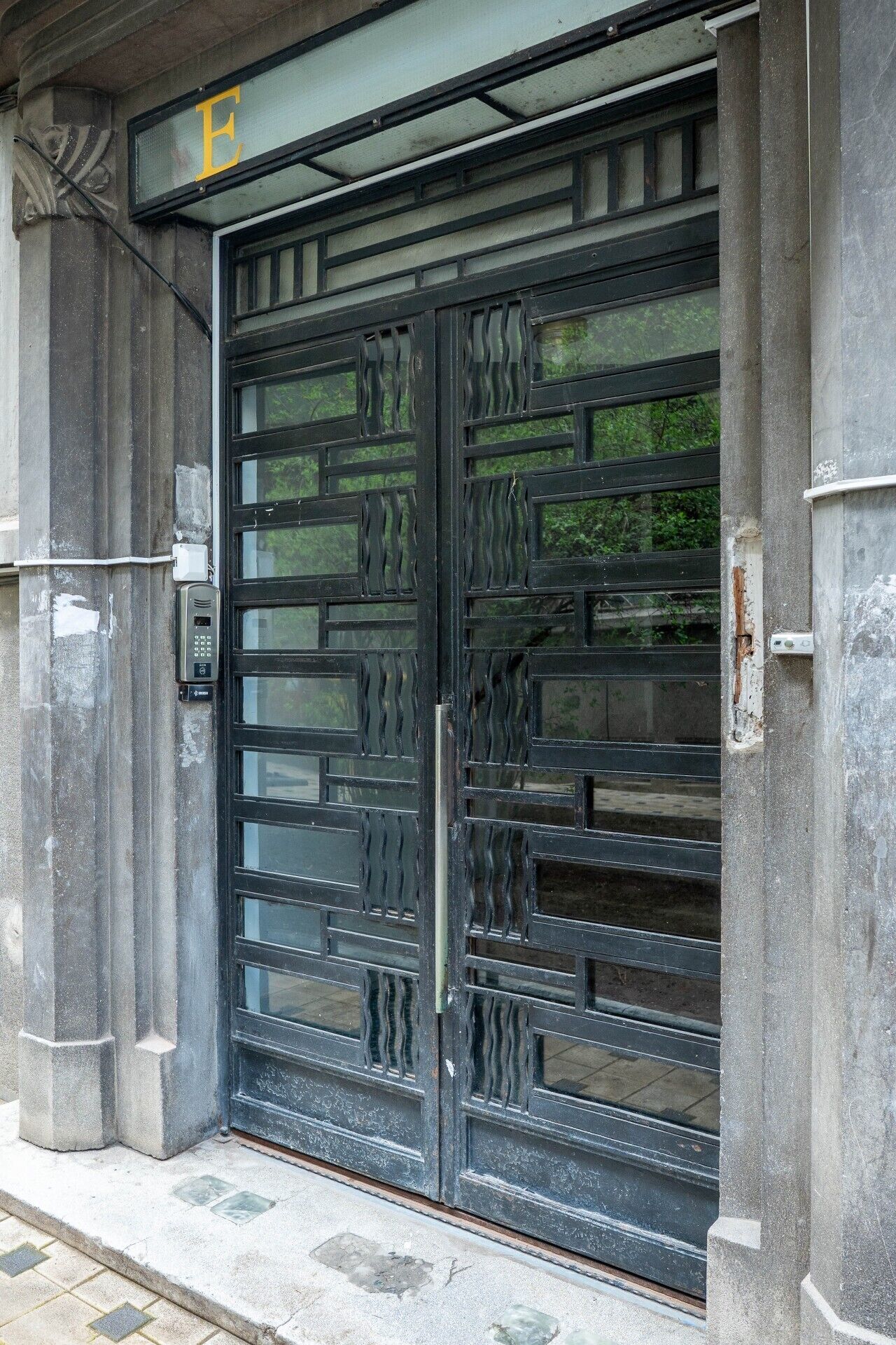 Une grande porte en métal ouvragée, surmontée d’un panneau de verre, le tout intégré à une structure en pierre.