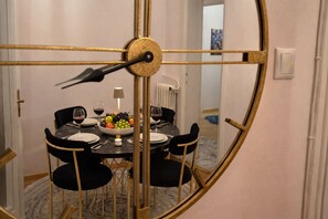 A dining area with a round table, black chairs, a fruit bowl, wine glasses, and a clock. - Luxury l Apartment | Radisson | Calea Victoriei (Bucharest)