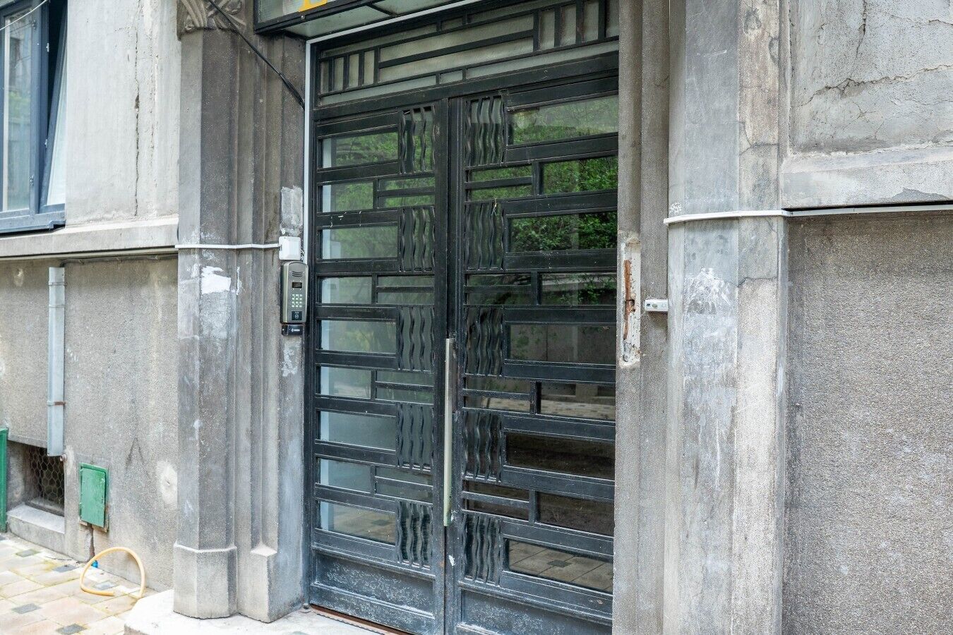 Una reja de metal negro con cerradura numérica, en una pared de concreto con marco de puerta verde.