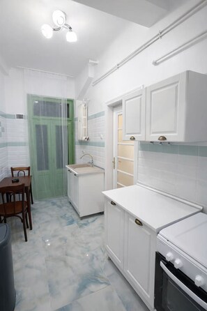 A kitchen with white cabinets, a stove, a sink, and a dining area with chairs. - Luxury l Apartment | Radisson | Calea Victoriei (Bucharest)