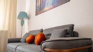 A grey sofa with two orange cushions, a teal floor lamp, and a colorful abstract painting on the wall. - Luxury l Apartment | Radisson | Calea Victoriei (Bucharest)