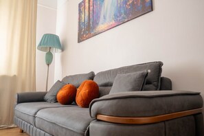 Ein graues Sofa mit zwei orangen Kissen, eine türkisfarbene Stehlampe und ein farbenfrohes abstraktes Gemälde an der Wand.