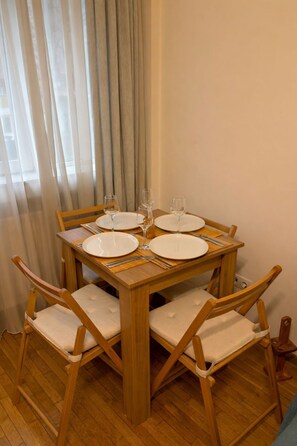 A dining table set for four with wooden chairs and a window with curtains. - Downtown Comfort Studio - Stay different (Bucharest)