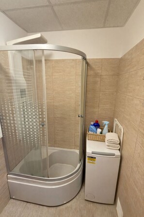 A shower enclosure with a glass door, a white towel, and a basket of toiletries. - Downtown Comfort Studio - Stay different (Bucharest)
