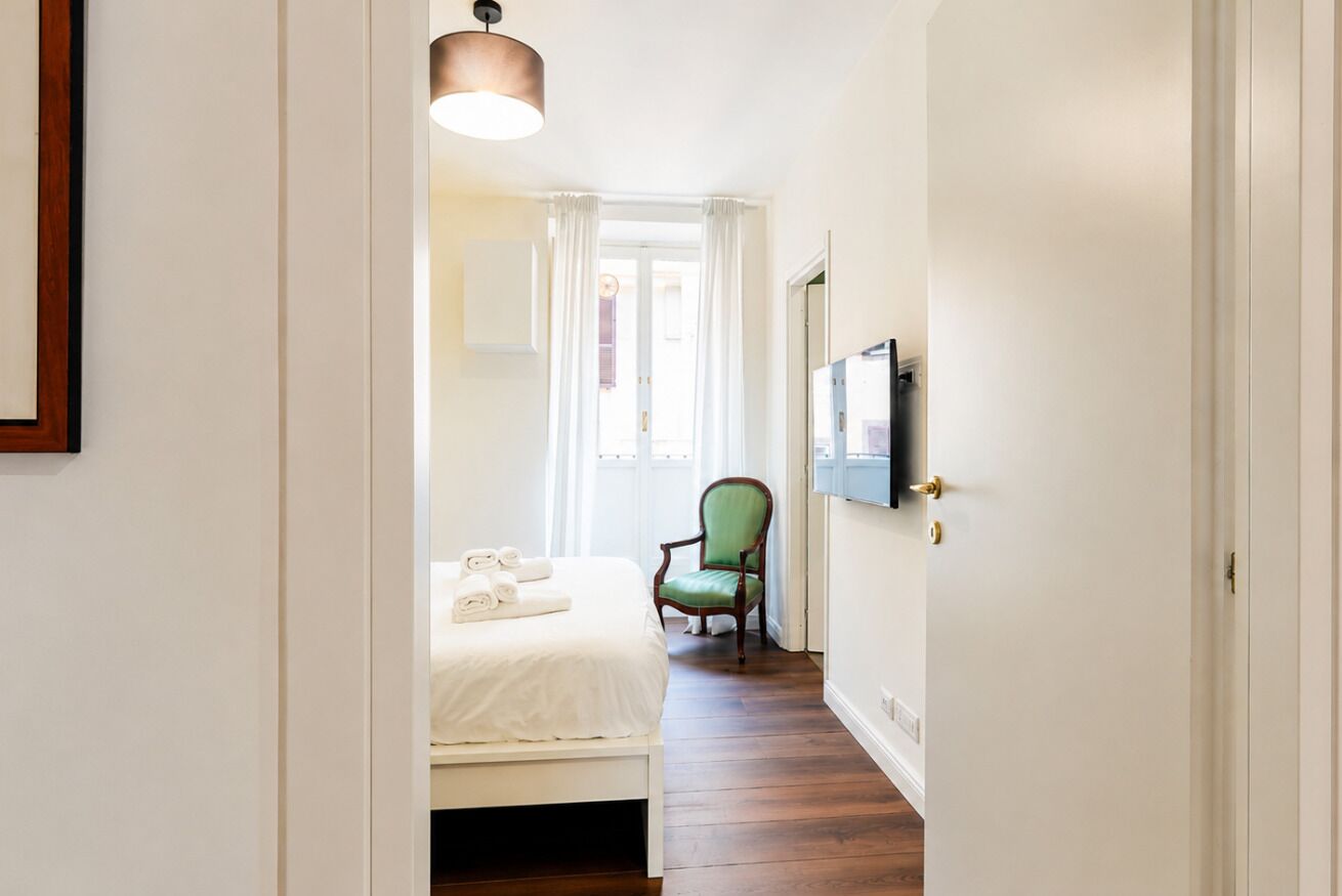 Et hotelværelse med seng, stol, fjernsyn og dør.
