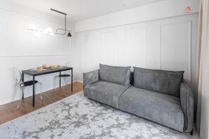 Ein modernes Wohnzimmer mit grauem Sofa, einem Esstisch mit Stühlen und einer Pendelleuchte.