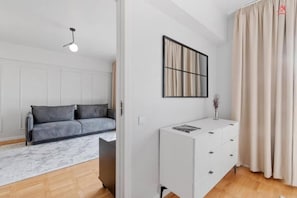 Ein modernes Zimmer mit einem grauen Sofa, einem weißen Schrank, einem gerahmten Kunstwerk und einem Fenster mit Vorhängen.