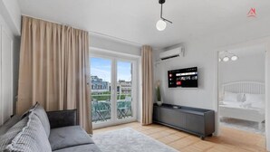 A modern living room with a sofa, a TV on the wall, and a balcony with a view of buildings. - Beautique Apartament Panoramic View | Central (Bucharest)