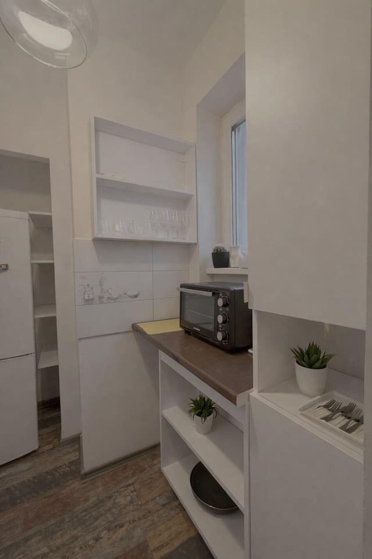 Une cuisine compacte équipée d’un grille-pain encastré, d’une petite fenêtre et d’une plante en pot.