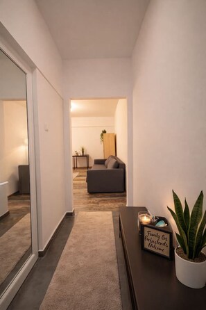 Ein Flur, der in einen Wohnbereich mit einer Couch, einem kleinen Tisch mit einem Schild und einer Topfpflanze führt.