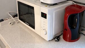 A microwave oven with a digital display, a red and black coffee maker, and a toaster on a countertop. - Modern Studio Apartment | Comfortable & Center (Bucharest)