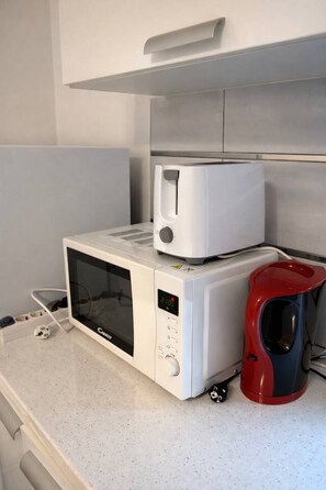 Un horno microondas con pantalla digital, una cafetera roja y negra y un tostador sobre una encimera.