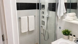A modern bathroom with a glass-enclosed shower, a white sink with a mirror, and a black and white tiled backsplash. - Modern Studio Apartment | Comfortable & Center (Bucharest)