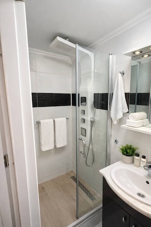 Un baño moderno con ducha de vidrio, lavamanos blanco con espejo y salpicadero de azulejos blanco y negro.