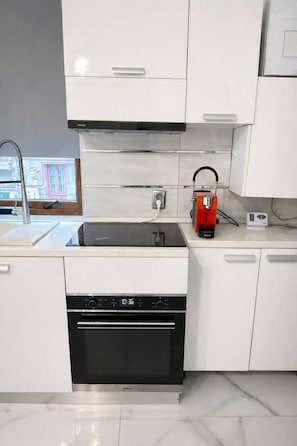 Cocina moderna con armarios blancos, lavavajillas negro, cafetera roja y pileta de acero inoxidable.
