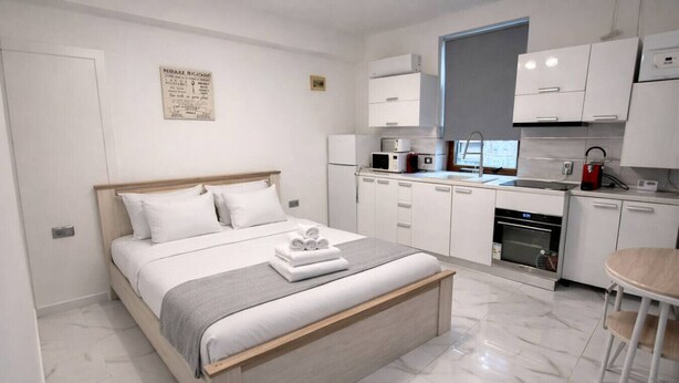 A modern bedroom with a bed, a bedside table, a small kitchen area with a microwave, and a dining area with a chair. - Modern Studio Apartment | Comfortable & Center (Bucharest)