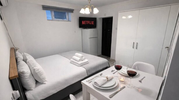 Ein modernes Hotelzimmer mit Bett, einem Fernseher, der 'NETFLIX' anzeigt, einem Esstisch mit Weingläsern und einem Kleiderschrank.