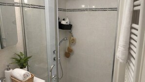 Ein modernes Badezimmer mit Duschkabine aus Glas, einem weißen Waschbecken mit Pflanze und einem Handtuchhalter.