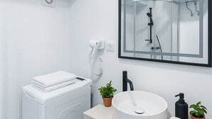 A modern bathroom with a built-in washing machine, a sink with a mirror above, and a shower enclosure. - Downtown Loft with Panoramic View (Bucharest)