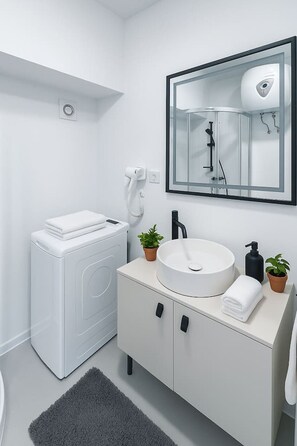 Ein modernes Badezimmer mit Waschmaschine, Waschbecken und Spiegel sowie einer Duschkabine.