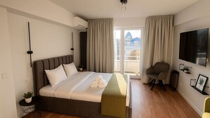 A modern hotel room with a bed, a chair, a TV, and a balcony with curtains. - Downtown Loft with Panoramic View (Bucharest)