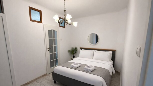 A modern bedroom with a bed, a chandelier, a round mirror, and a door with frosted glass panels. - LightHouse Apartment | 2 BedRoom Apartment (Bucharest)