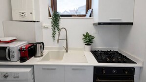A compact kitchen with a white countertop, a stainless steel sink, a gas stove, a microwave, and a small potted plant. - LightHouse Apartment | 2 BedRoom Apartment (Bucharest)