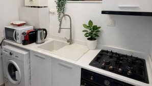A compact kitchen with a washing machine, microwave, sink, and stove. - LightHouse Apartment | 2 BedRoom Apartment (Bucharest)